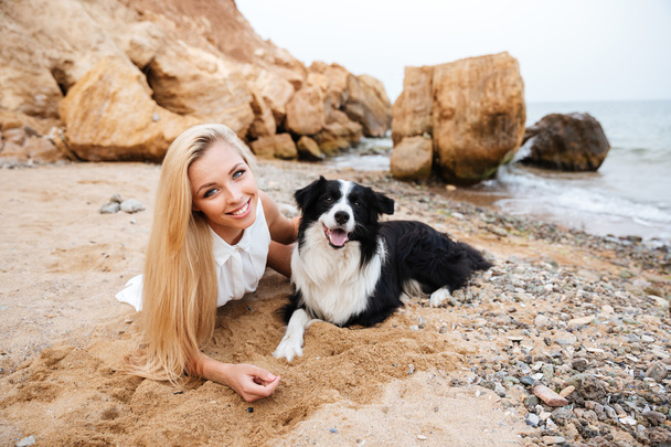 Happy young woman relaxing with her dog on the beach - Foto, imagen