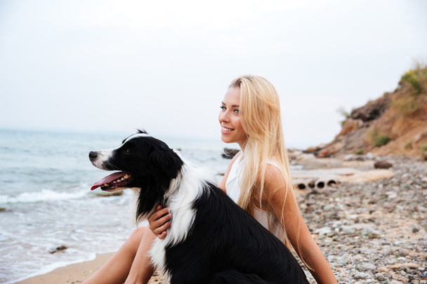 Smiling woman with dog sitting on the beach and thinking - Foto, imagen
