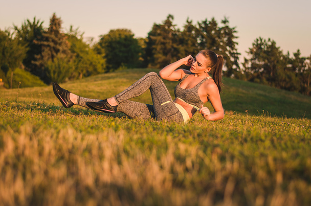 Fitness atraente jovem mulher sentada na grama em um parque fazer
 - Foto, Imagem
