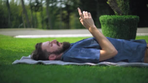 Człowiek odpoczywa za pomocą smartfona na otwartym powietrzu. - Materiał filmowy, wideo