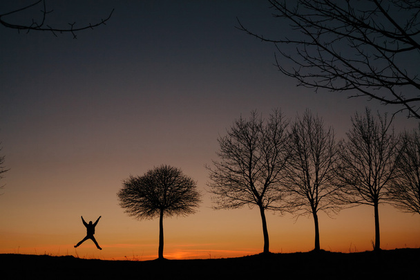 silhouet van een man die bij zonsondergang springt - Foto, afbeelding