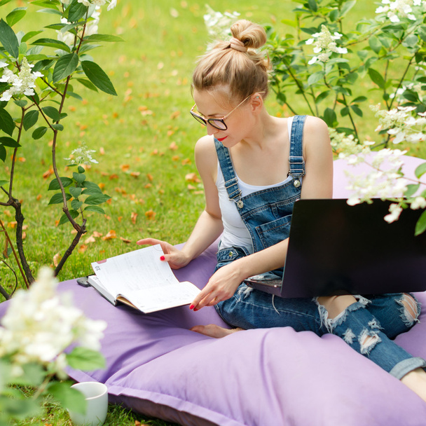Freelancer työskentelee puutarhassa. Kirjoittaminen, surffaaminen internetissä. Nuori nainen rentouttava ja hauskaa puistossa juo kahvia. Etäopetus, freelance-käsite
. - Valokuva, kuva