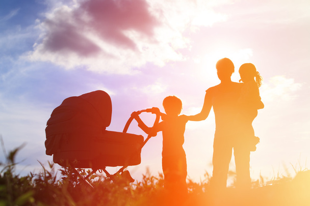 Silhueta de mãe com três filhos andando ao pôr do sol, família feliz
 - Foto, Imagem