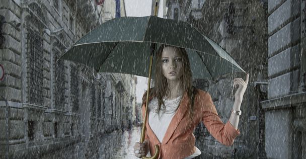 Beautiful woman with umbrella in town under rain - Фото, изображение