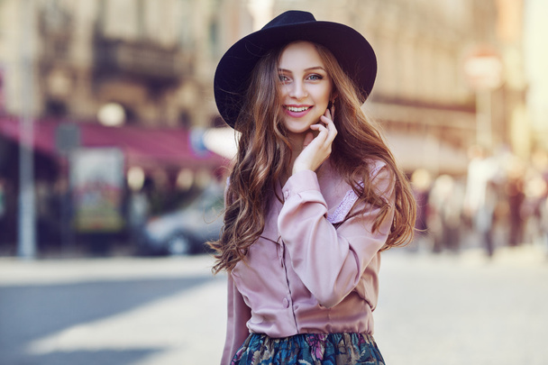 Außenporträt einer jungen schönen modischen glücklichen Dame, die auf der Straße posiert. Modell mit stylischem Hut mit breiter Krempe und Kleidung. Mädchen blickt in die Kamera. Damenmode. Lebensstil in der Stadt - Foto, Bild