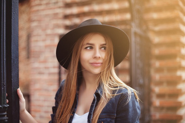 Portrait of beautiful fashionable girl wearing stylish wide-brimmed black hat looking up. City lifestyle. Toned - Фото, изображение