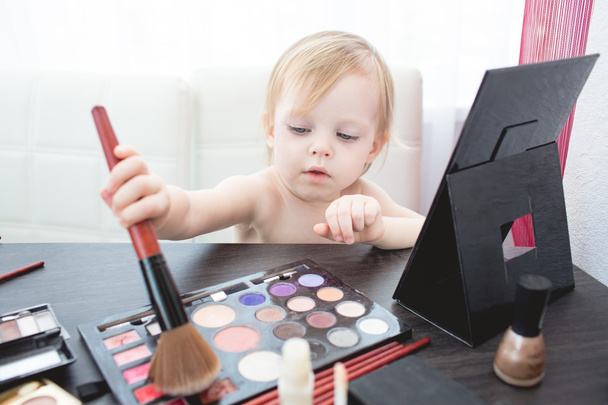 Cute little girl with cosmetics and mirror. - Foto, afbeelding