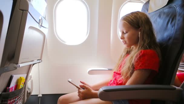Entzückendes kleines Mädchen, das mit dem Flugzeug unterwegs ist. Kind hört Musik am Flugzeugfenster - Filmmaterial, Video