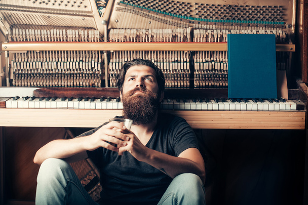 bearded man with glass near wood piano - Foto, afbeelding