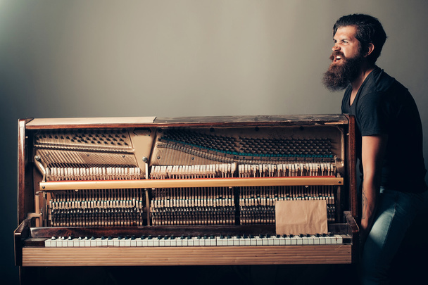 bearded man trying to move wooden piano - Foto, imagen