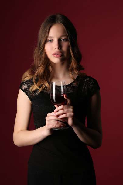 Girl in dress holding glass of wine. Close up. Dark red background - Фото, изображение