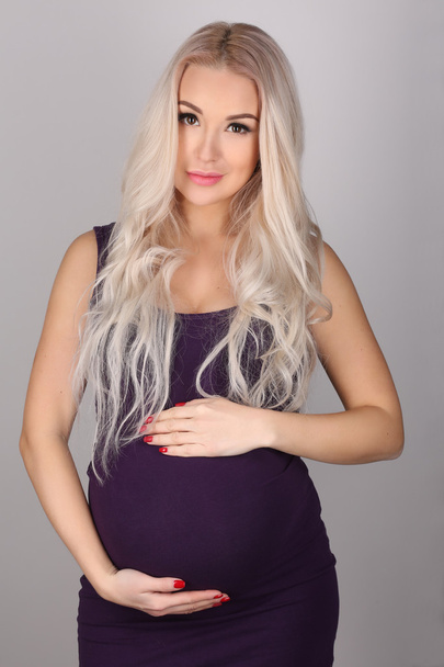 Pregnant woman with long hair holding her belly. Close up. Gray background - Foto, Bild