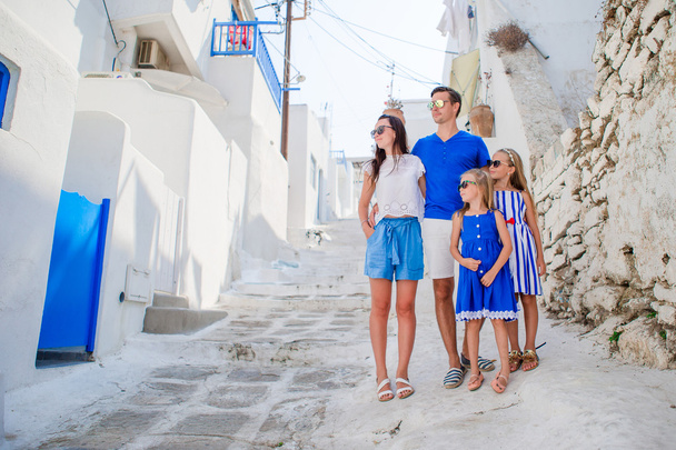 Family vacayion in Europe. Parents and kids at street of typical greek traditional village with white walls and colorful doors on Mykonos Island, in Greece - Photo, Image