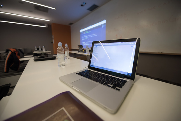 leeg klaslokaal met programmacode op projectorscherm en moderne laptopcomputers op tafel - Foto, afbeelding