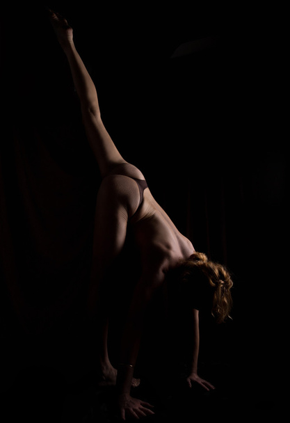 Back view of beautiful female bottom, naked body on a black background. slim woman doing yoga asanas - Foto, Imagem
