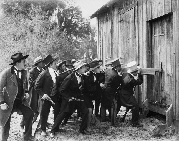 Группа людей в пушках и шляпах вламывается в сарай
 - Фото, изображение