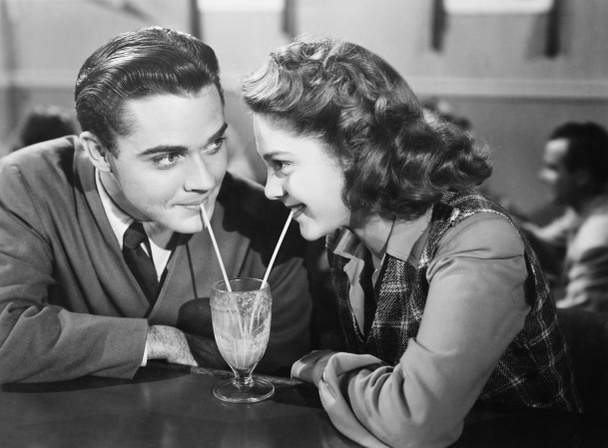 Couple dans un restaurant se regardant et partageant un milk shake avec deux pailles
 - Photo, image