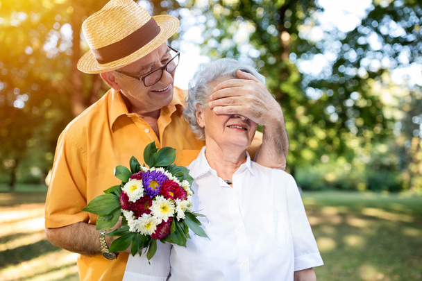 Senior man boeket van gekleurde bloemen te geven aan zijn vrouw - Foto, afbeelding