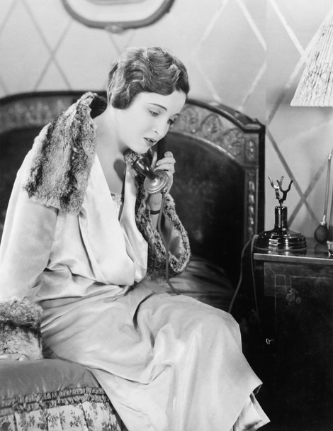 Young woman sitting on her bed in the bed room, speaking on the telephone - Photo, Image