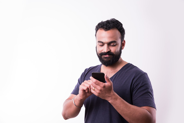 хипстер индийский молодой человек с бородой и усами занят с помощью смартфона, изолированных на белом фоне
 - Фото, изображение