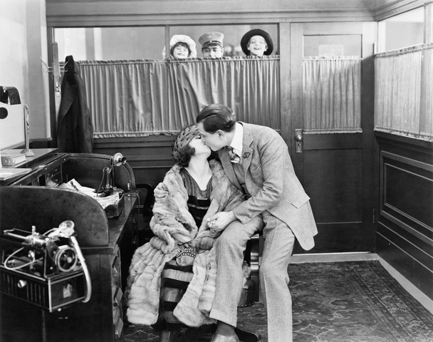 Paar küsst sich im Büro, während Kinder und ein Bote über einen Vorhang blicken - Foto, Bild