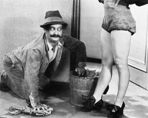 Homem limpando o chão olhando para as pernas de uma mulher
 - Foto, Imagem