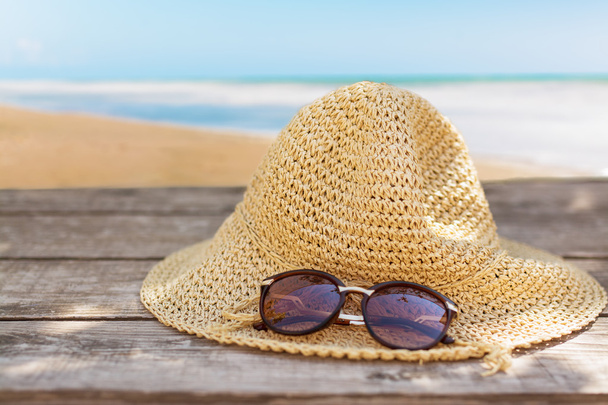 fedora hat and sunglasses over wooden table and sea landscape background. - Фото, изображение