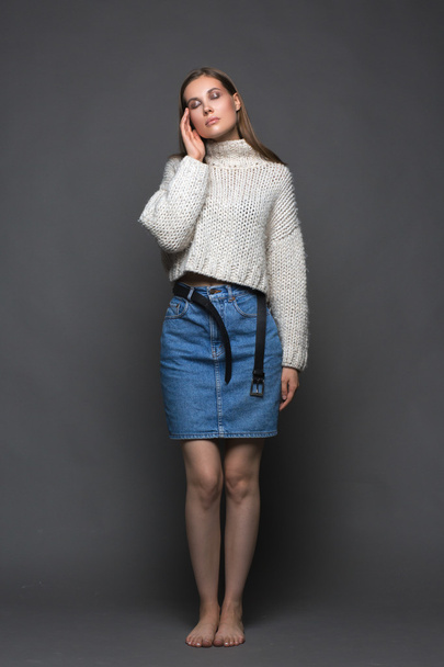 Portrait of beauty young woman in white fashion female pullover and blue jeans skirt on gray background - Foto, Imagen