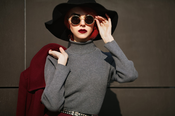 Closeup portré fiatal szép divatos nő napszemüveg. Hölgy, aki sötétszürke háttérrel pózol. Modell visel, stílusos, széles karimájú kalap. Lány látszó-on fényképezőgép. Női divat. Tónusú - Fotó, kép