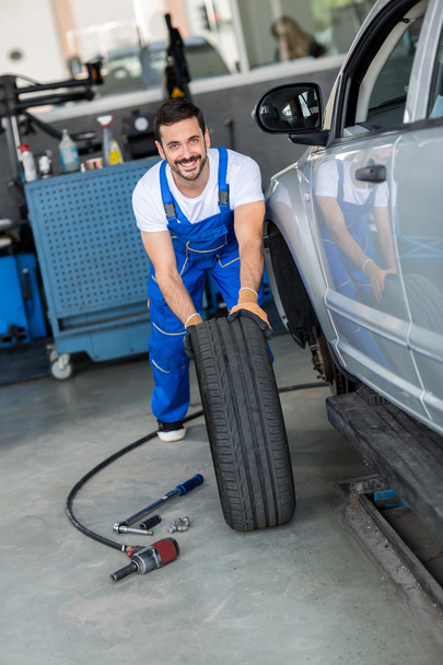 smiling mechanic repair and  pushing a black tyre - Photo, image