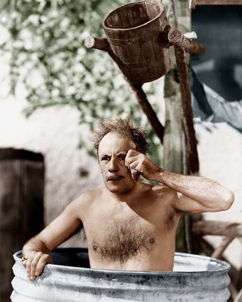 Mies istuu tynnyrissä kylvyssä ja katselee monokkeliaan.
 - Valokuva, kuva