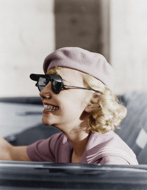 Fiatal nő a svájcisapka, és napszemüveg, egy autó, útközben - Fotó, kép