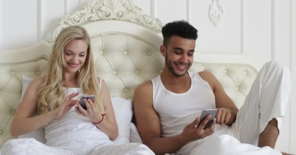 Couple lying bed using smart phone, mix race man woman smile morning bedroom - Materiaali, video