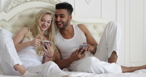 Couple lying bed using smart phone, mix race man woman smile morning bedroom - Metraje, vídeo