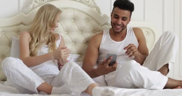 Couple lying bed using smart phone, mix race man woman smile morning bedroom - Πλάνα, βίντεο