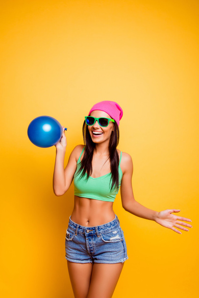 Cheerful hipster girl in pink hat holding balloon near yellow wa - Foto, Imagen