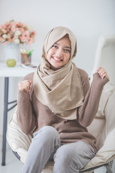 excited young woman with hijab smiling while sitting on a couch - Foto, Imagem