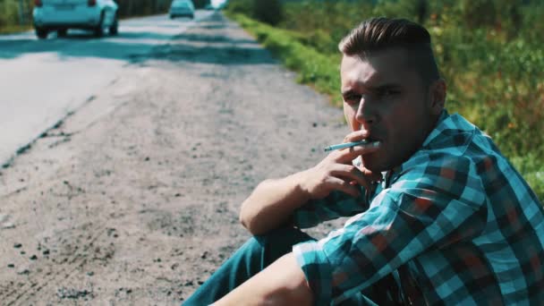 Az ember ül road, vidéken. A stoppolással. Vár. Cigaretta a dohányzás. - Felvétel, videó