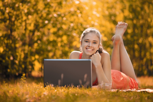 Jeune femme avec ordinateur portable dans le parc sur l'herbe, en automne
 - Photo, image