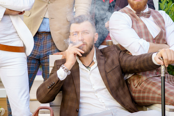 Successful young elegant man relaxing with friends and smoking cigar - Фото, изображение