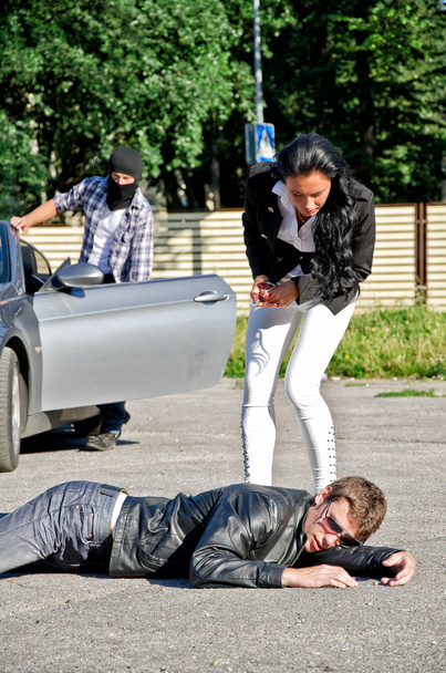 Male thief stealing a car while his accomplice distracts female driver - 写真・画像