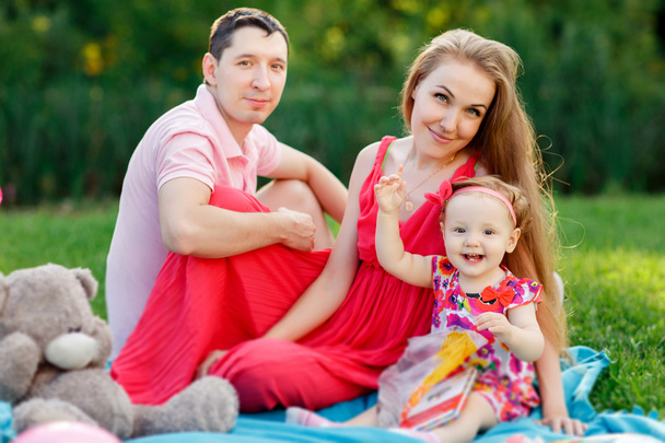 Young parents with daughter and book sitting on plaid - Foto, Imagem