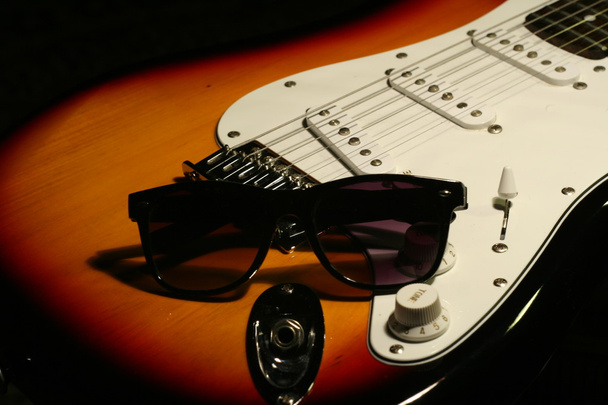 Винтажная электрогитара с солнечными очками на черном фоне
 - Фото, изображение
