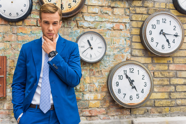 Man in suit standing near wall with clocks - Foto, Imagen