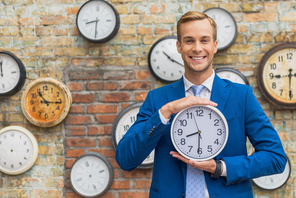 Man in suit standing near wall with clocks - Foto, afbeelding