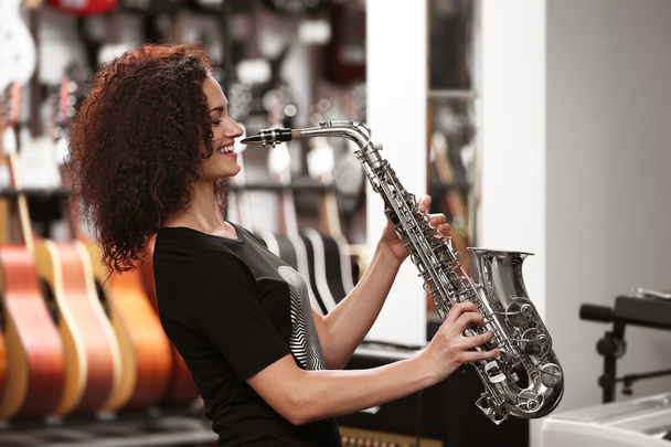 Beautiful girl playing saxophone in music shop - Фото, зображення