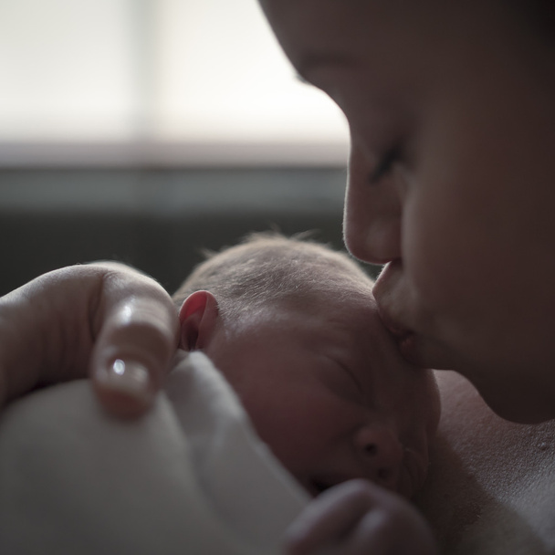 Мать дарит новорожденному малышу поцелуи в родильном зале больницы
 - Фото, изображение