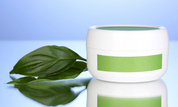 Jar of cream with green leaves on blue background - Φωτογραφία, εικόνα