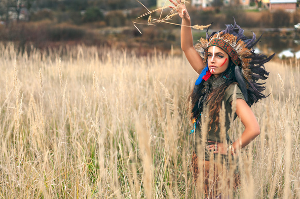 Girl dressed in native American Indian clothes throw up wheat ears in the field - Фото, зображення