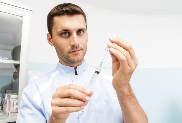 young male doctor prepares a medicine into the syringe in the office.Doctor holding a syringe - Zdjęcie, obraz